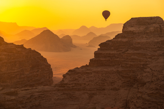 Aerial view of a hot air balloon floating over the sandstone mountains and desert landscape during a golden sunset in Wadi Rum Aqaba Governorate Jordan.