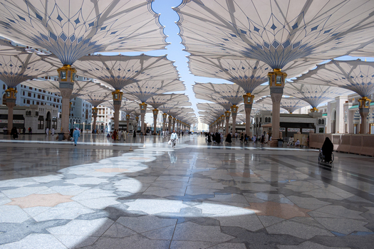 View of the large retractable umbrellas providing shade in the courtyard of Al Masjid e Nabawi with people walking on the patterned marble floor in Madinah Al Madinah Province Saudi Arabia.