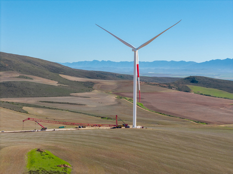 Aerial view of a wind turbine standing in rolling agricultural fields under a clear blue sky with a construction crane at its base in Swellendam Western Cape South Africa. Aerial view of a wind turbine standing in rolling agricultural fields under a clear blue sky with a construction crane at its base in Swellendam Western Cape South Africa.