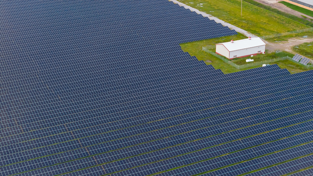 Aerial view of a large solar farm with rows of photovoltaic panels and a small white building in a grassy field in Saginaw Michigan United States.