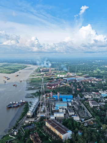 Aerial view of the Karnaphuli River flowing past an industrial power plant with ships docked along the banks surrounded by lush greenery in Chattogram Chittagong Division Bangladesh.