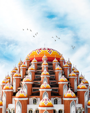 Aerial view of Masjid Kubah 99 Asmaul Husna with colorful domes and intricate architecture under a blue sky with birds in Kecamatan Mariso Sulawesi Selatan Indonesia.
