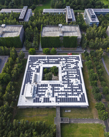Aerial view of HTC 33 building at High Tech Campus Eindhoven featuring a large rooftop solar array and a central green courtyard surrounded by lush forest in Eindhoven Noord Brabant Netherlands. Aerial view of HTC 33 building at High Tech Campus Eindhoven featuring a large rooftop solar array and a central green courtyard surrounded by lush forest in Eindhoven Noord Brabant Netherlands.