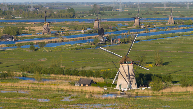 Aerial view of the historic Kinderdijk windmills standing along blue canals in the lush green polder landscape under bright sunlight Kinderdijk South Holland Netherlands. Aerial view of the historic Kinderdijk windmills standing along blue canals in the lush green polder landscape under bright sunlight Kinderdijk South Holland Netherlands.