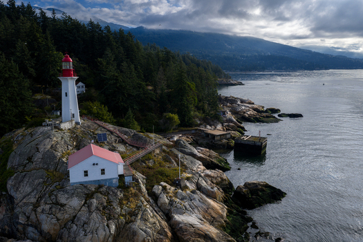 Aerial view of Point Atkinson Lighthouse Federal Heritage Building situated on a rocky coastline surrounded by dense evergreen forest in West Vancouver British Columbia Canada.