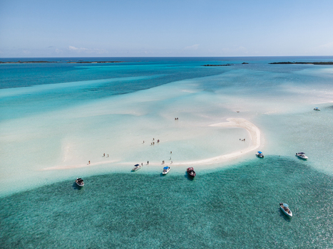 Aerial view of people walking on the white sand of Man O War Cay Sandbar surrounded by turquoise water and anchored boats in Rolletown Exuma The Bahamas. Aerial view of people walking on the white sand of Man O War Cay Sandbar surrounded by turquoise water and anchored boats in Rolletown Exuma The Bahamas.