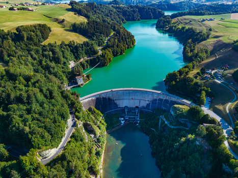 Aerial view of Barrage de Rossens dam spanning the Sarine River surrounded by green hills forests and turquoise waters of Lac de la Gruyere in Pont la Ville Fribourg Switzerland.