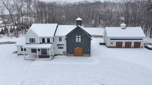 Aerial view of a modern farmhouse with a dark grey and white exterior a detached three car garage and a snow covered yard in Shrewsbury Massachusetts United States. Aerial view of a modern farmhouse with a dark grey and white exterior a detached three car garage and a snow covered yard in Shrewsbury Massachusetts United States.