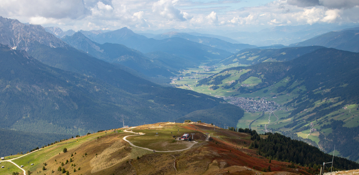 Aerial view of the Dolomites mountain range featuring lush green slopes winding paths and a distant valley village Rocca Pietore Veneto Italy.