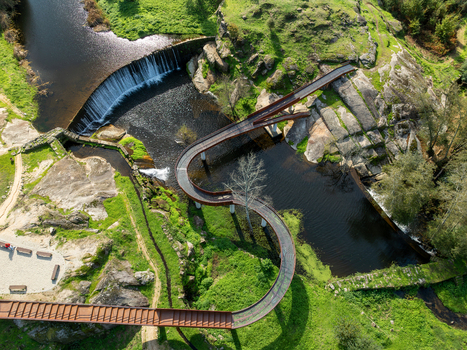 Aerial view of Acude da Ribeira with its winding wooden walkway over the river and small waterfall surrounded by rocky terrain and green grass in Ervedal Coimbra Portugal. Aerial view of Acude da Ribeira with its winding wooden walkway over the river and small waterfall surrounded by rocky terrain and green grass in Ervedal Coimbra Portugal.