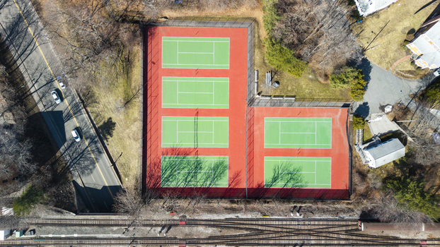 Aerial view of vibrant green tennis courts contrasting against the red base nestled beside a road and train tracks Braintree Massachusetts United States.