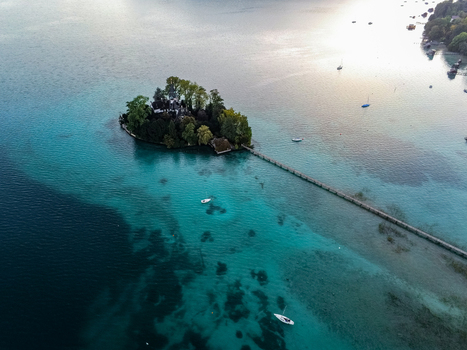 Aerial view of Schlossinsel island with its historic building and long wooden pier surrounded by the turquoise waters of Attersee in Vocklabruck District Upper Austria Austria.