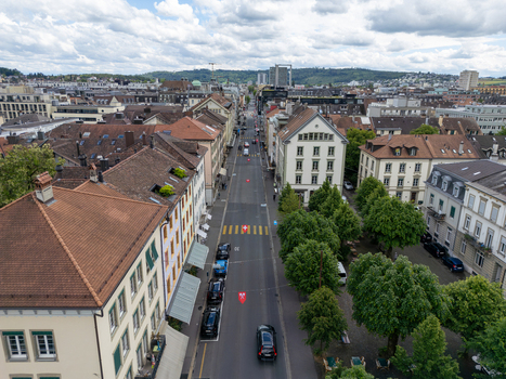Aerial view of historic buildings with red tiled roofs along a straight city street lined with green trees under a cloudy sky in Biel Bienne Canton of Bern Switzerland. Aerial view of historic buildings with red tiled roofs along a straight city street lined with green trees under a cloudy sky in Biel Bienne Canton of Bern Switzerland.