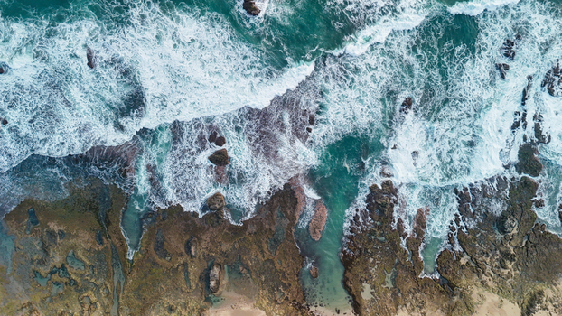 Aerial view of the rugged coastline with crashing waves turquoise water and rocky formations along the shore in Indonesia. Aerial view of the rugged coastline with crashing waves turquoise water and rocky formations along the shore in Indonesia.