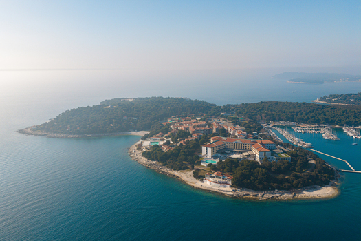 Aerial view of a sun kissed peninsula with terracotta rooftops nestled among emerald trees bordered by the turquoise Adriatic Sea Pula Istria County Croatia.