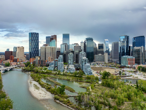 Aerial view of the Calgary skyline featuring modern skyscrapers the Bow River and lush greenery under a cloudy sky in Calgary Alberta Canada.