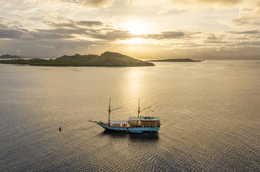 Aerial view of a traditional wooden phinisi boat anchored in the calm waters near Komodo Island at sunset with golden light reflecting on the sea in Komodo East Nusa Tenggara Indonesia.