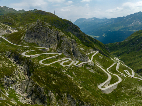 View of the winding Sankt Gotthard Pass road snaking through the lush green mountains and rocky slopes Airolo Ticino Switzerland.