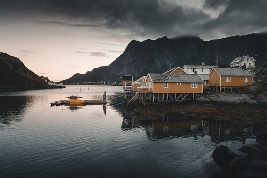 Moskenes Nordland Norway 08 September 2022 View of Sakrisoya with its iconic yellow rorbuer cabins on stilts over the water set against dramatic dark mountains under a moody twilight sky. Moskenes Nordland Norway 08 September 2022 View of Sakrisoya with its iconic yellow rorbuer cabins on stilts over the water set against dramatic dark mountains under a moody twilight sky.
