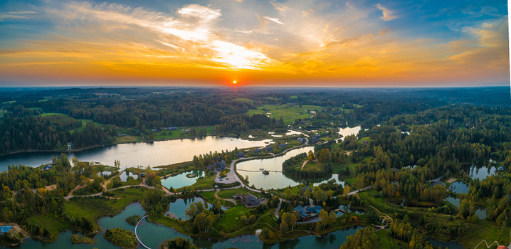 Aerial view of a serene landscape featuring interconnected lakes dense forests and rolling green hills illuminated by the warm glow of a sunset in Latvia. Aerial view of a serene landscape featuring interconnected lakes dense forests and rolling green hills illuminated by the warm glow of a sunset in Latvia.
