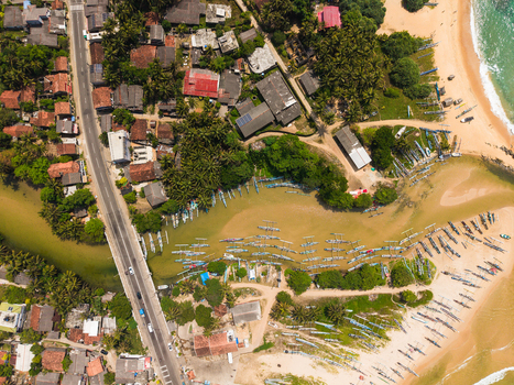 Aerial view of traditional outrigger boats parked on the sandy beach and in the lagoon near a coastal village with palm trees and houses in Dodanduwa Southern Province Sri Lanka. Aerial view of traditional outrigger boats parked on the sandy beach and in the lagoon near a coastal village with palm trees and houses in Dodanduwa Southern Province Sri Lanka.