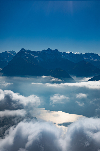 Aerial view of the Swiss Alps with snow capped peaks rising above a sea of clouds and a sunlit lake below in Airolo Ticino Switzerland. Aerial view of the Swiss Alps with snow capped peaks rising above a sea of clouds and a sunlit lake below in Airolo Ticino Switzerland.