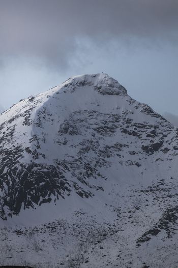 View of a rugged snow covered mountain peak under a dark cloudy sky in the arctic wilderness Kvaloya Troms Norway. View of a rugged snow covered mountain peak under a dark cloudy sky in the arctic wilderness Kvaloya Troms Norway.