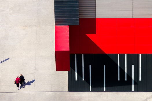 Aerial view of two people walking on a concrete plaza beside a modern building with striking red and black geometric panels in Belgrade City of Belgrade Serbia. Aerial view of two people walking on a concrete plaza beside a modern building with striking red and black geometric panels in Belgrade City of Belgrade Serbia.