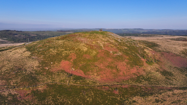 Aerial view of Chapelle Saint Michel de Brasparts atop a hill surrounded by reddish moorland and green vegetation under a clear blue sky in Saint Rivoal Bretagne France. Aerial view of Chapelle Saint Michel de Brasparts atop a hill surrounded by reddish moorland and green vegetation under a clear blue sky in Saint Rivoal Bretagne France.