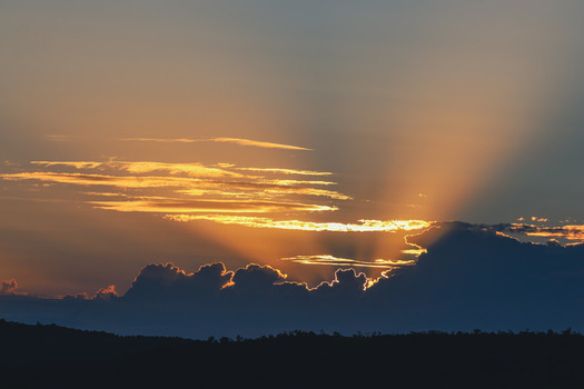 View of golden sunbeams breaking through dark clouds over the silhouetted horizon of the Welgevonden Game Reserve in Waterberg District Municipality Limpopo South Africa. View of golden sunbeams breaking through dark clouds over the silhouetted horizon of the Welgevonden Game Reserve in Waterberg District Municipality Limpopo South Africa.