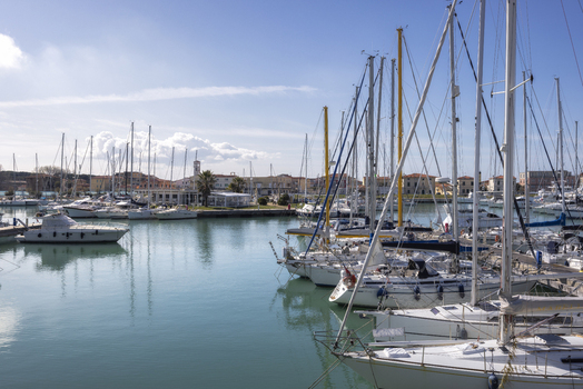 View of sailboats and yachts moored in the harbor with coastal buildings under a clear blue sky in Marina di Pisa Tuscany Italy.