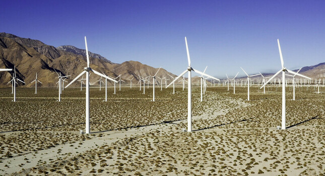 Aerial view of wind turbines stretching across a dry desert landscape under a clear blue sky in Palm Springs CA United States.