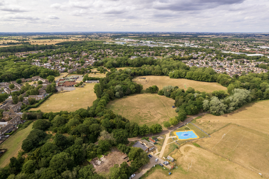 Aerial view of Bretton Park featuring lush green spaces mature trees a blue play area and surrounding residential neighborhoods in Peterborough England United Kingdom. Aerial view of Bretton Park featuring lush green spaces mature trees a blue play area and surrounding residential neighborhoods in Peterborough England United Kingdom.