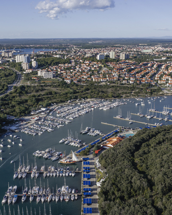 Aerial view of the marina at Pjescana Uvala with sailboats and yachts docked in the harbor surrounded by lush forests and the urban landscape of Pula Istarska zupanija Croatia.
