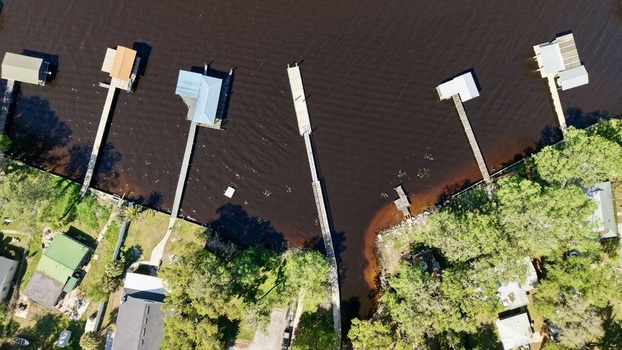 Aerial view of Sixmile Creek featuring wooden docks and boathouses extending into dark water surrounded by lush green trees and houses in St. Johns County Florida United States.