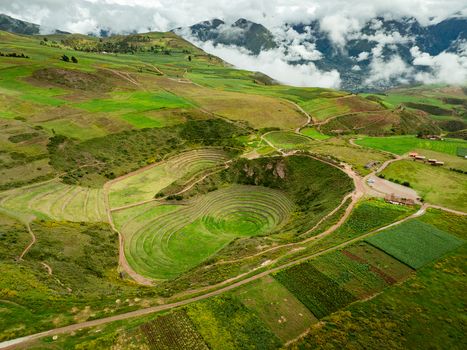 Aerial view of the ancient Inca agricultural terraces at Zona Arqueologica Moray featuring circular stone lined depressions set within the lush green landscape near Maras Cuzco Peru.
