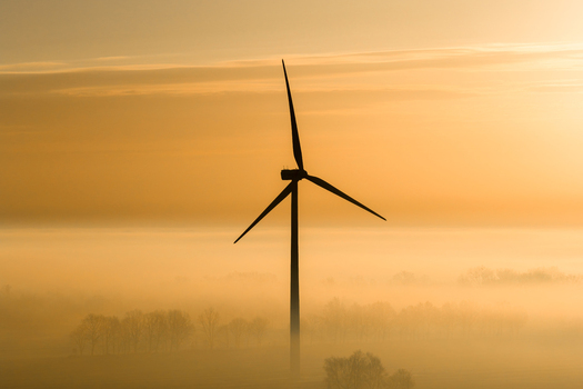 Aerial view of a solitary wind turbine piercing the misty landscape its blades silhouetted against the golden sunrise creating a serene yet powerful scene Wislina Pomeranian Voivodeship Poland. Aerial view of a solitary wind turbine piercing the misty landscape its blades silhouetted against the golden sunrise creating a serene yet powerful scene Wislina Pomeranian Voivodeship Poland.