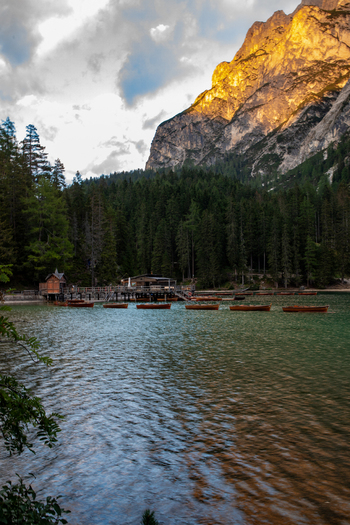 View of wooden boats on a lake in the Dolomites with a dense pine forest and mountain peaks illuminated by golden hour light in Rocca Pietore Veneto Italy. View of wooden boats on a lake in the Dolomites with a dense pine forest and mountain peaks illuminated by golden hour light in Rocca Pietore Veneto Italy.