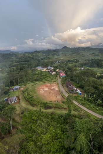 Aerial view of the Bangka Kenda school grounds with a dirt playground surrounding lush green hills and a rainbow in the sky in Wae Rii East Nusa Tenggara Indonesia.