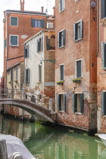 View of a quiet canal in Venice with the historic Ponte delle Turchette bridge traditional orange hued buildings with green shutters and calm water in Venice Veneto Italy. View of a quiet canal in Venice with the historic Ponte delle Turchette bridge traditional orange hued buildings with green shutters and calm water in Venice Veneto Italy.