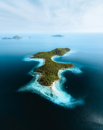 Aerial view of the lush green island of Coron surrounded by vibrant turquoise coral reefs and deep blue ocean waters in Coron Mimaropa Philippines.