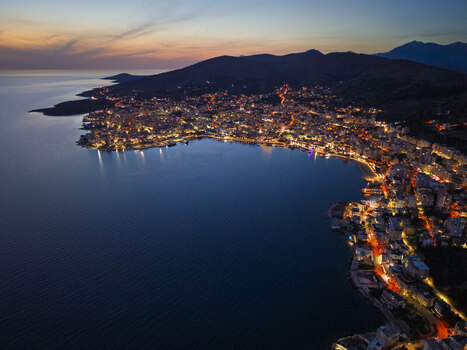 Aerial view of the illuminated coastal city of Saranda at twilight featuring glowing streetlights along the bay dense urban architecture and dark mountains in Saranda Vlore County Albania. Aerial view of the illuminated coastal city of Saranda at twilight featuring glowing streetlights along the bay dense urban architecture and dark mountains in Saranda Vlore County Albania.
