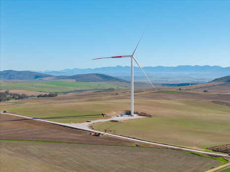 Aerial view of a large wind turbine standing in a vast agricultural landscape with rolling hills and distant mountains under a clear blue sky Swellendam Western Cape South Africa. Aerial view of a large wind turbine standing in a vast agricultural landscape with rolling hills and distant mountains under a clear blue sky Swellendam Western Cape South Africa.