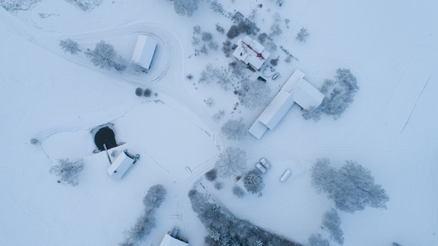 Aerial view of a snow covered rural landscape featuring farm buildings scattered trees and a frozen pond Latvia. Aerial view of a snow covered rural landscape featuring farm buildings scattered trees and a frozen pond Latvia.