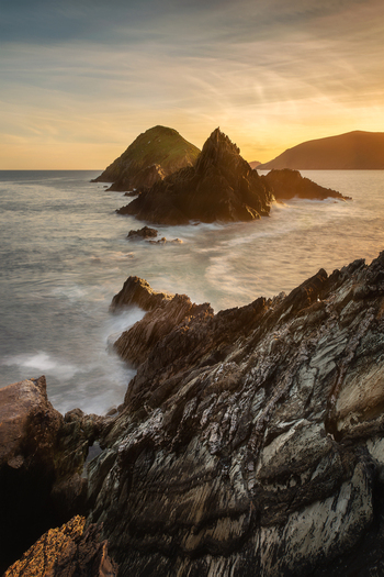 View of the rugged cliffs and rocky outcrops of Dunmore Head at sunset with waves crashing against the rocks in Ireland.
