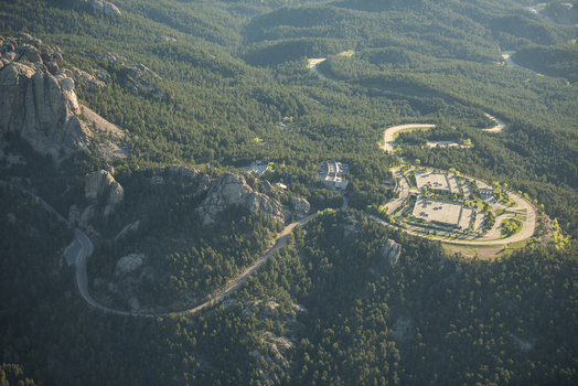 Aerial view of Mount Rushmore National Memorial surrounded by dense pine forests winding roads and parking facilities in Keystone South Dakota United States. Aerial view of Mount Rushmore National Memorial surrounded by dense pine forests winding roads and parking facilities in Keystone South Dakota United States.