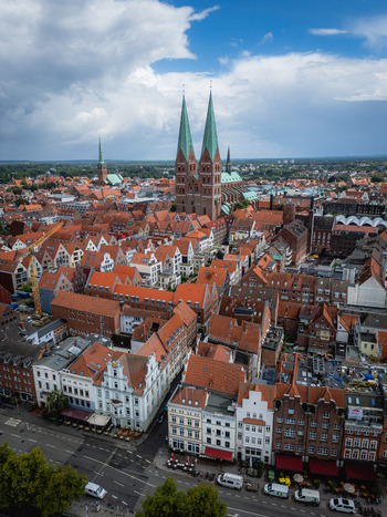 Aerial view of red tiled roofs nestle closely together punctuated by the soaring twin spires of the L&uuml;beck Cathedral against a backdrop of a clouded sky L&uuml;beck Schleswig Holstein Germany.