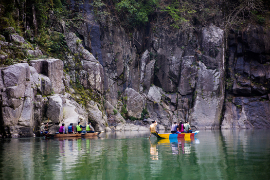 Meghalaya India 31 March 2023 View of people in colorful wooden boats on the clear water of the Umngot River surrounded by towering rocky cliffs. Meghalaya India 31 March 2023 View of people in colorful wooden boats on the clear water of the Umngot River surrounded by towering rocky cliffs.