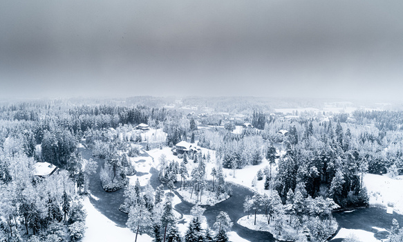 Aerial view of a snow covered forest landscape with a winding frozen river and scattered houses under a cloudy winter sky in Latvia. Aerial view of a snow covered forest landscape with a winding frozen river and scattered houses under a cloudy winter sky in Latvia.