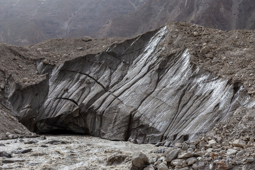 View of the rugged Baltoro Glacier with deep crevasses and rocky moraine formations above a flowing glacial meltwater river in Baltoro Gilgit Baltistan Pakistan.